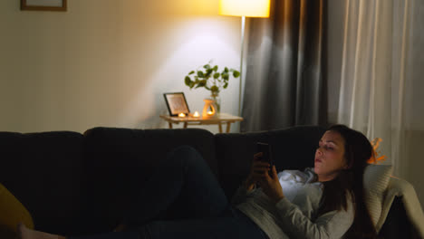 Woman-Lying-On-Sofa-At-Home-At-Night-Streaming-Or-Looking-At-Online-Content-On-Mobile-Phone-3